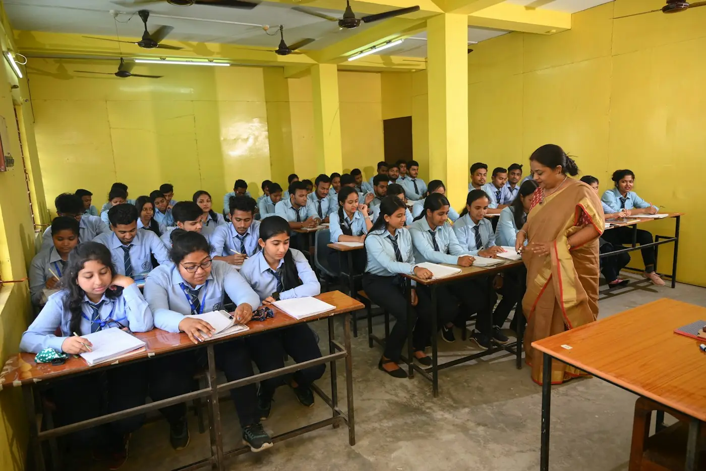 A teacher walking between rows of students working in class.